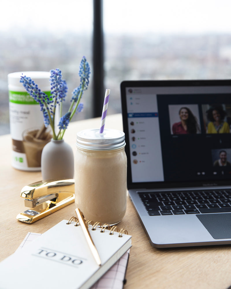 
                  
                    Load image into Gallery viewer, Herbalife Nutrition Formula 1 shake in a glass jar with striped straw on a home office desk, beside laptop, flowers, and to-do list.
                  
                